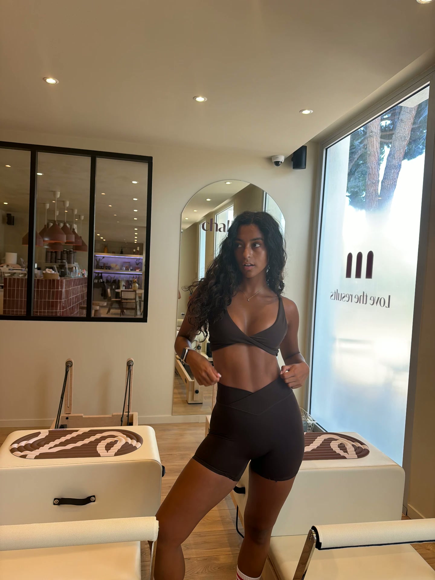 Layza Venancio standing between reformer machines in a sunlit boutique studio
